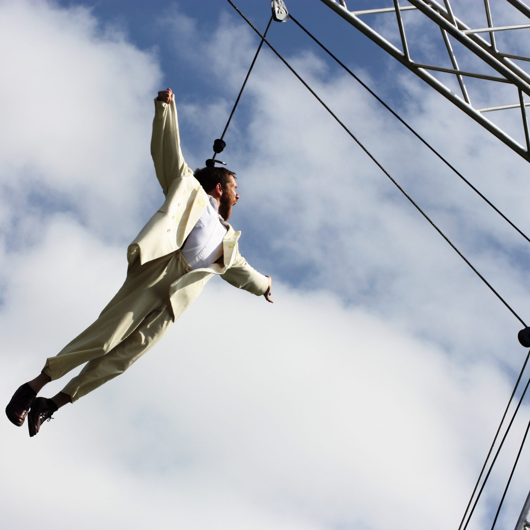 Jamie flying on an aerial harness in the Weighting show. His arms are stretched out to the sides in joy.