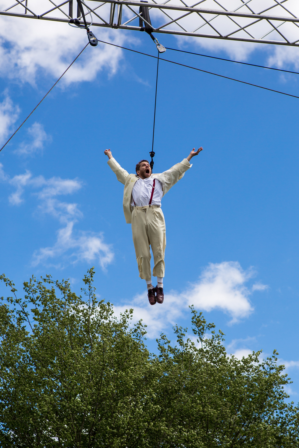 Jamie flies on a harness, his arms outstretched in joy, a bright blue sky behind him.