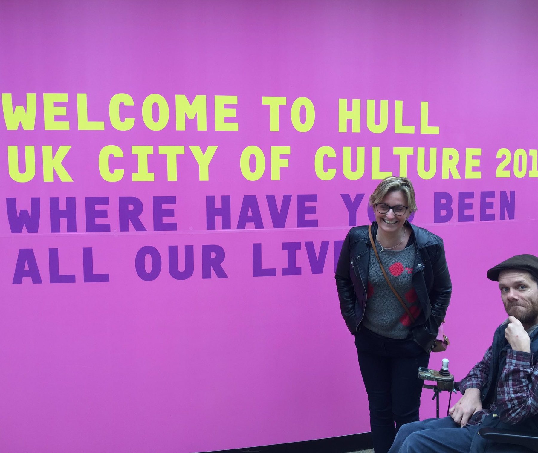 Jamie and Claire in front of a big purple sign that reads 'Welcome to Hull UK city of culture 2017. Where have you been all our lives?'