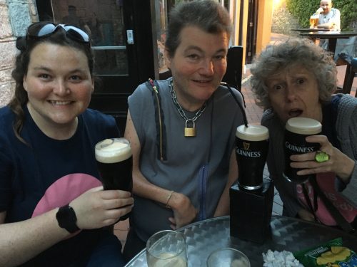 Eilis, Joh and Spicer sit at a table in an Irish pub holding pints of Guinness and grinning