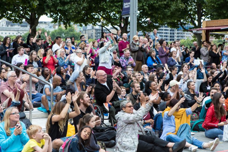 An audience outside at The National Theatre, cheering and applauding with smiles - Extraordinary Bodies performance What Am I Worth