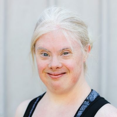 Helen poses for the camera. She is a young white woman with bleached blonde hair tied back. She has bright blue eyes and is wearing a sporty sleeveless top.