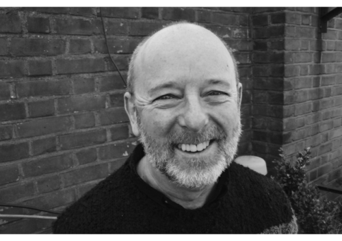 Headshot of Willie, a white man in his fourties with a bright smile and a grey-white beard and a shaved head.